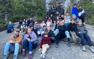 Students and teachers sit on the side of a mountain for a photo together.