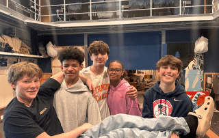 A group of students hold up another in their arms for a group photo.