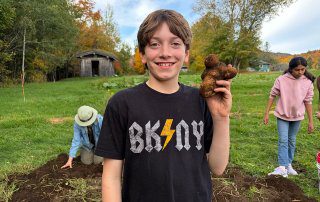 Young boy holds a potato he harvested in his hand. It has a unique shape.
